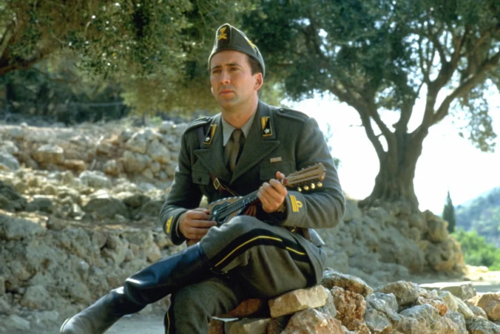 Nicolas Cage as Captain Corelli, wearing a vintage military uniform and holding a mandolin, standing against a sunny Greek island landscape.