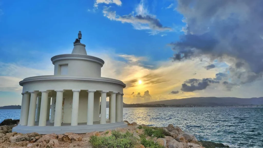 A close-up view of the white circular Doric colonnade of the Fanari lighthouse in Argostoli during a vibrant sunset.