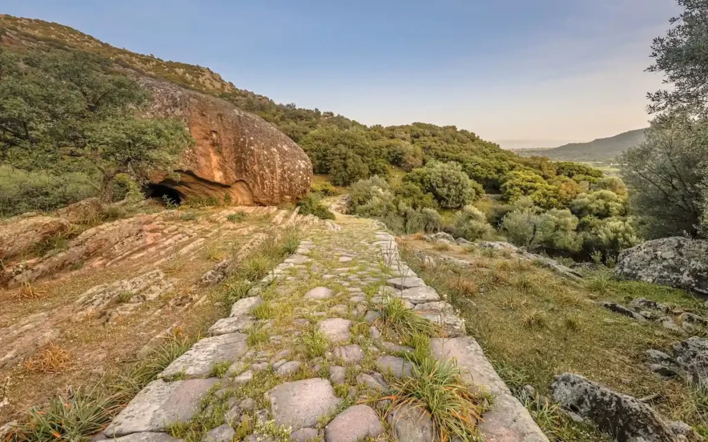 A wide, open-air walkway made of weathered fieldstones, cutting through a natural landscape.