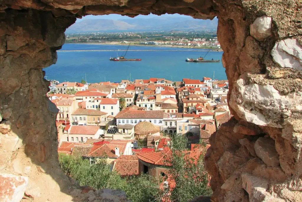 A high-altitude view looking down from a stone fortress onto the city of Nafplio and the sea.