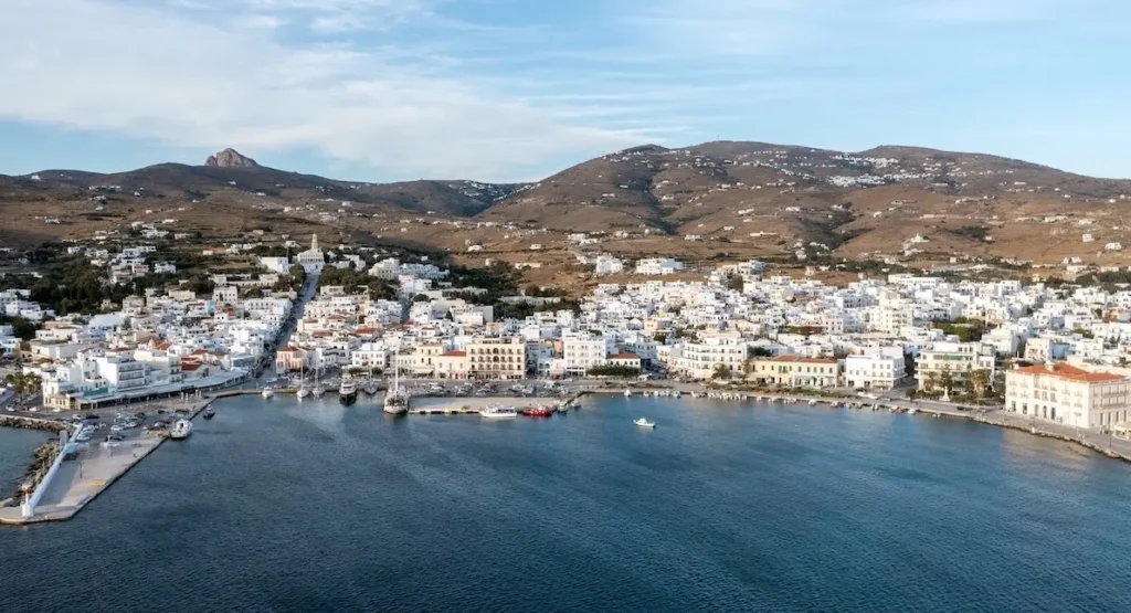 An aerial view of Tinos Town harbor with the road leading to the Church of Panagia and the granite peak of Exomvourgo in the distance.