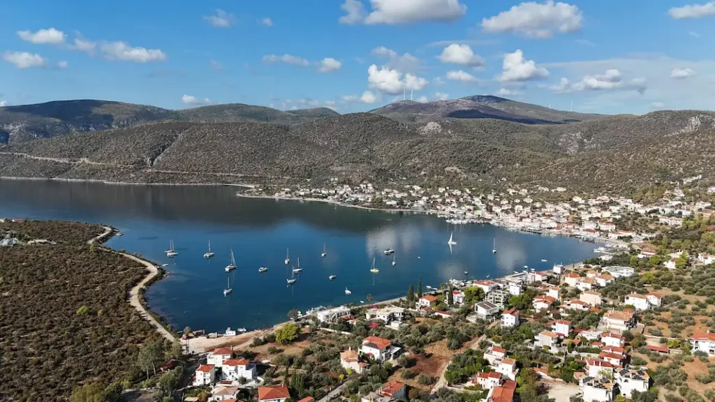 High-angle aerial view of Korfos village in Corinthia, showing the sheltered bay, waterfront tavernas, and traditional Greek seaside architecture.