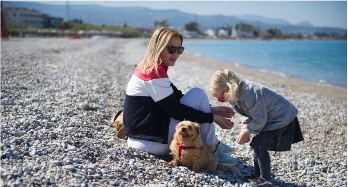 Real estate agent Nikol Lafazani on a sunny beach in Corinthia with a toddler and a dog, representing the family-friendly lifestyle in Greece.