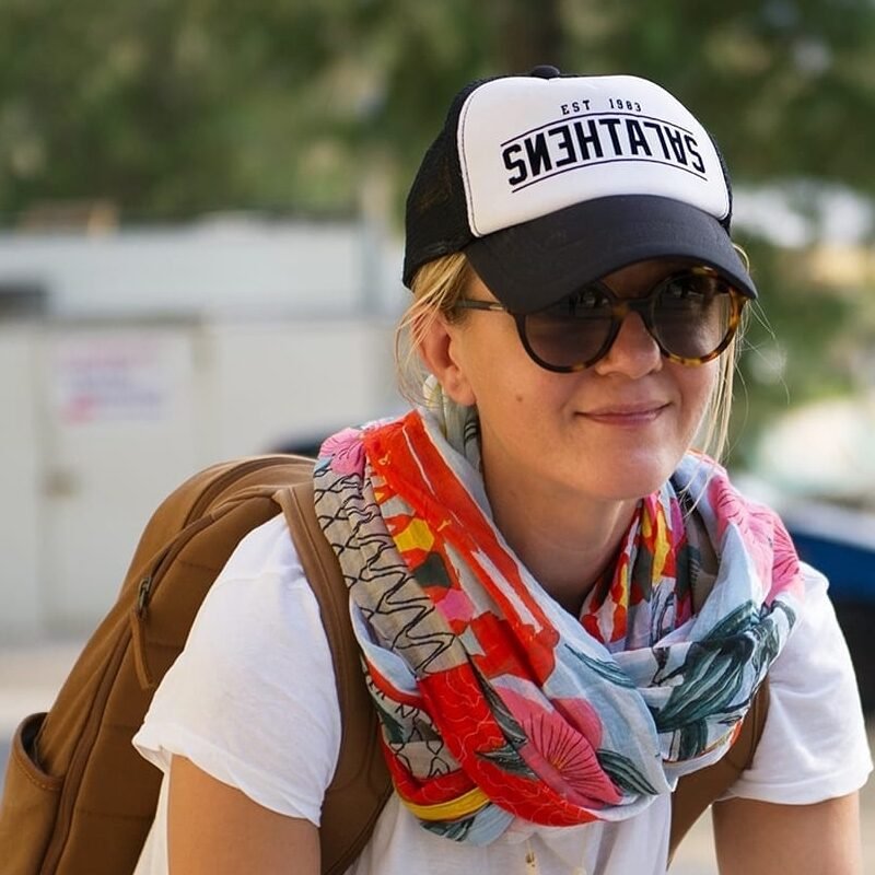 Portrait of Nikol Lafazani on a bicycle in a coastal Greek town, highlighting the bike-friendly infrastructure of the Corinthia region.