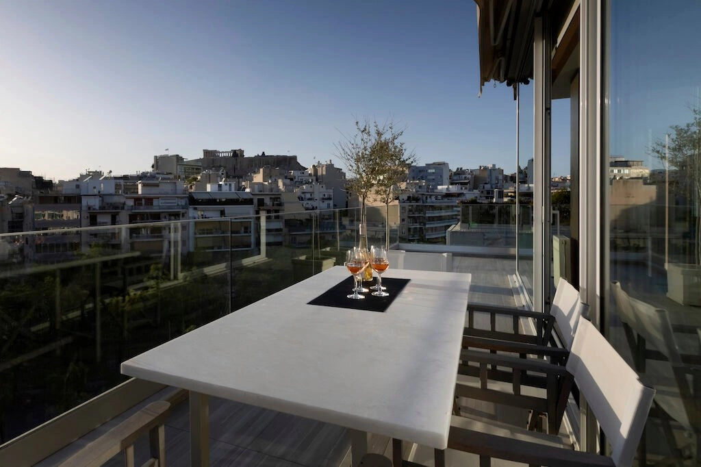 A beautifully set dinner table on a private balcony overlooking the illuminated Acropolis in Athens, Greece, during twilight.