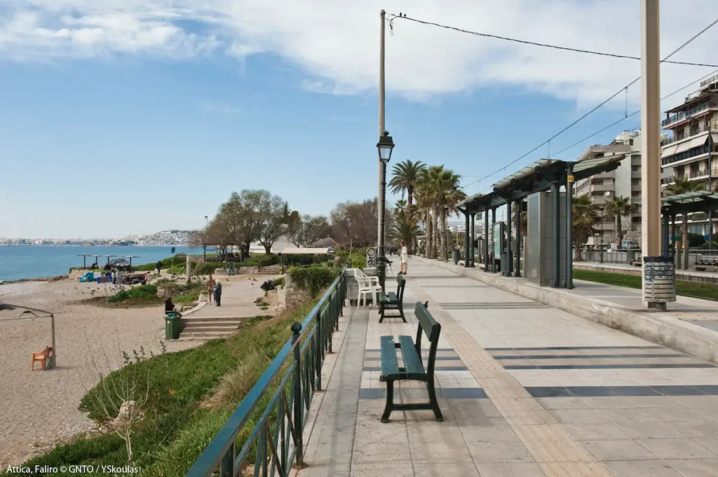 A wooden bench positioned along the Palaio Faliro seafront overlooking the sand and the Saronic Gulf.