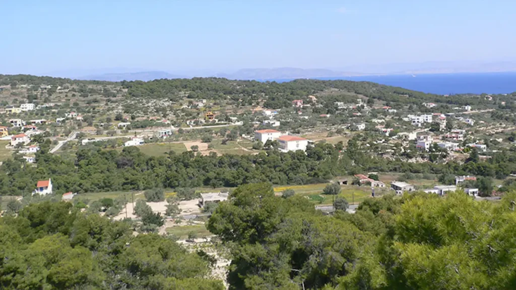 An aerial perspective of the village of Messagros showing scattered white houses amidst dense olive groves and pine forests near the Temple of Aphaia.