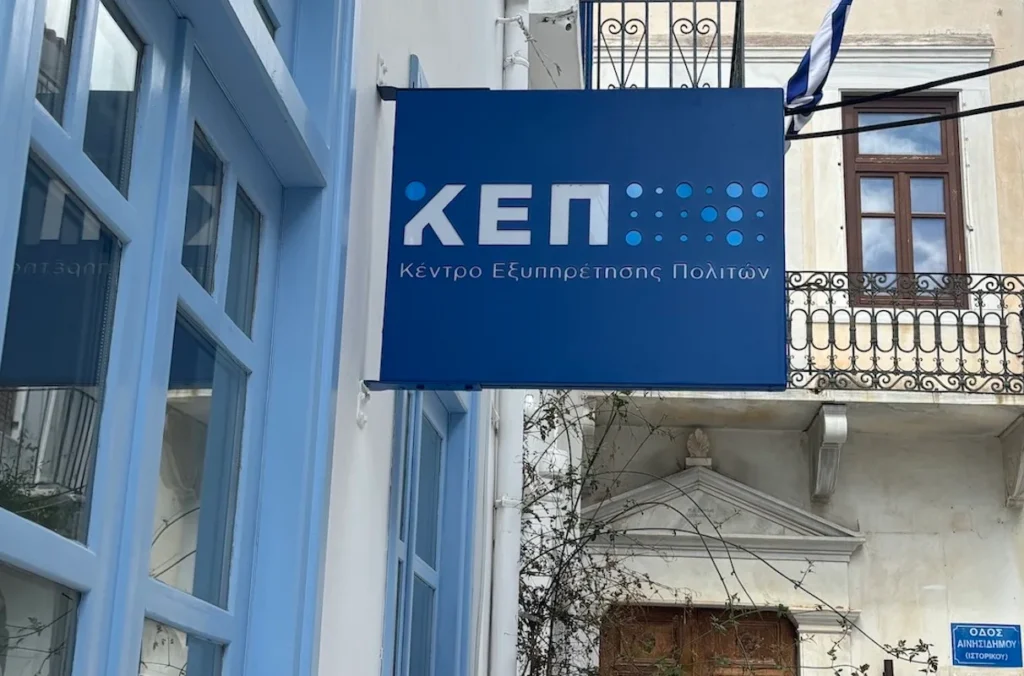 A traditional building on a Greek island with a blue and white sign for the KEP Citizens’ Service Centre, featuring a wooden door and potted plants at the entrance.
