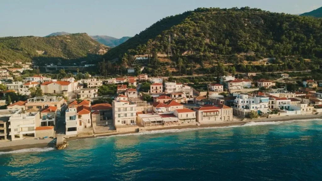 An aerial landscape view showing the village of Derveni nestled between the Gulf of Corinth and the lush green mountains.