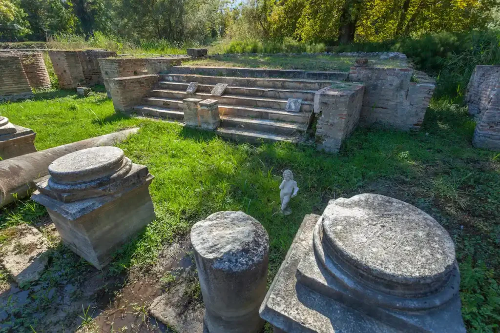 The foundation and scattered marble fragments of the Temple of Zeus Olympicus in Dion, surrounded by lush vegetation.