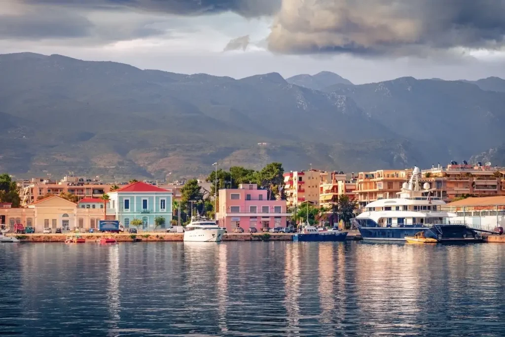 A row of grand, two-story neoclassical mansions with ornate balconies and large windows, situated along the Kalamata coastal road.