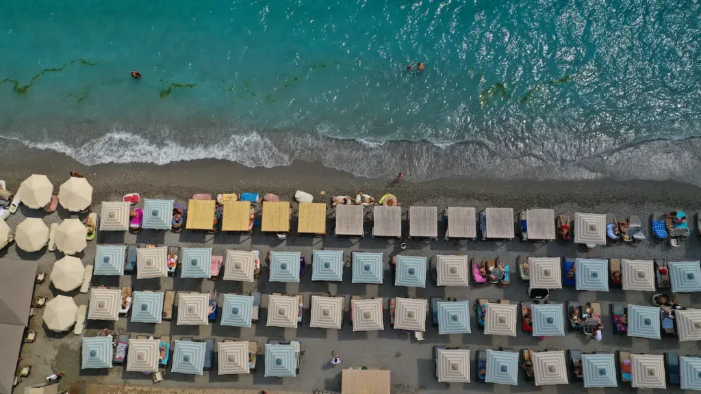A perspective shot from a section of the Kalamata city beach with sunbeds, showing colorful personal beach umbrellas and towel space, with the organized sunbed section visible in the distance.