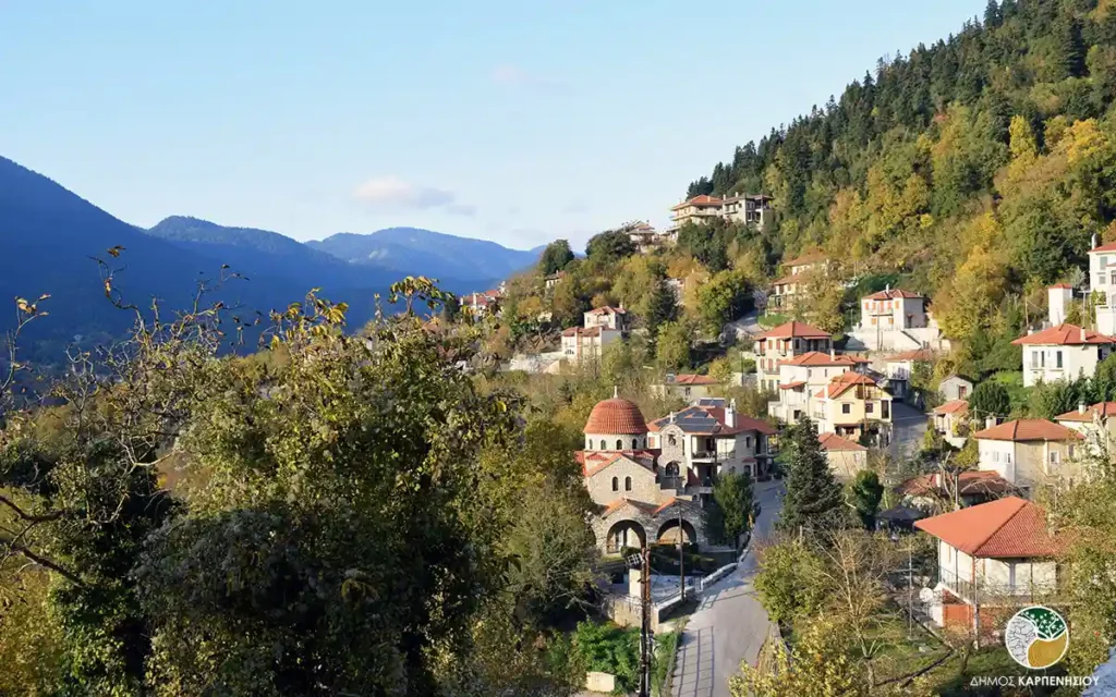 A snow-covered traditional village with stone houses nestled against a steep, dramatic mountain backdrop in Evrytania.