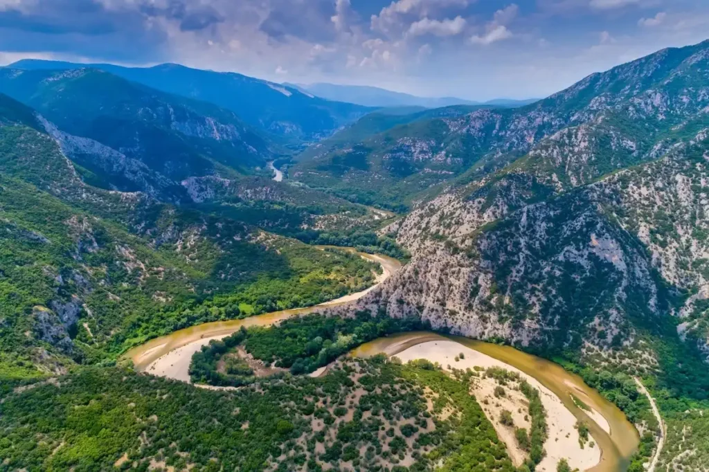 Aerial view of the winding Nestos River cutting through a deep, green limestone gorge with hiking paths along the cliffside.