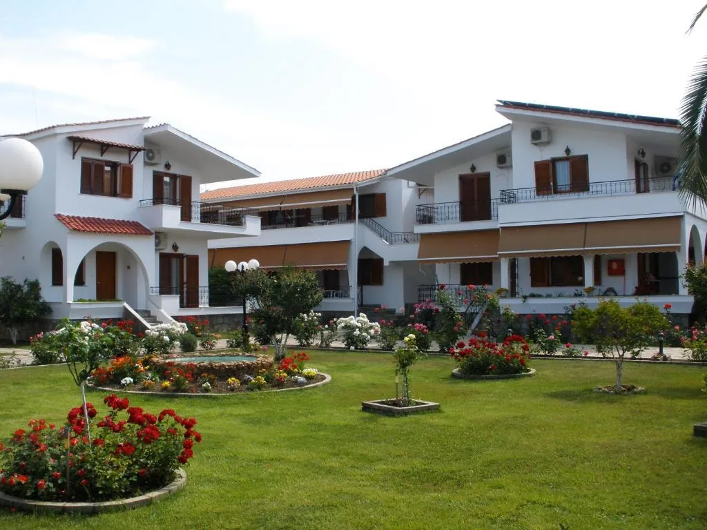The interior courtyard and landscaped garden of a modern two-story apartment building in Keramoti, showing paved paths and Mediterranean plants near the beach.