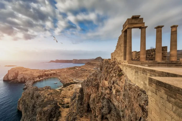 Scenic view of the circular bay beneath the ruins of Lindos, featuring turquoise water and rocky shores.