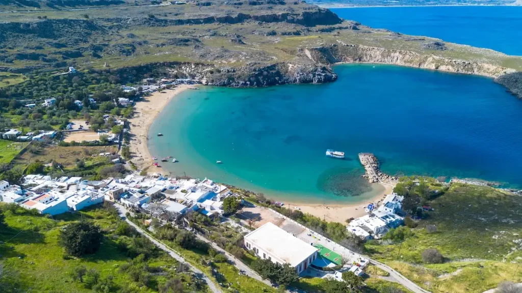 Scenic view of the circular bay beneath the ruins of Lindos, featuring turquoise water and rocky shores.