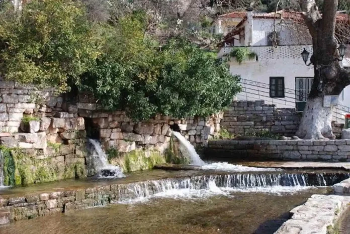 The historic Klepsidra spring in the central square of Mavromati, featuring flowing water from stone-carved outlets.