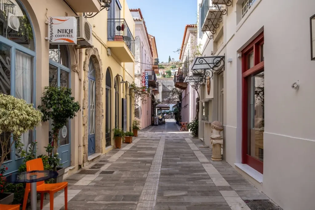 A narrow street lined with restored two-story neoclassical buildings featuring balconies and shutters.