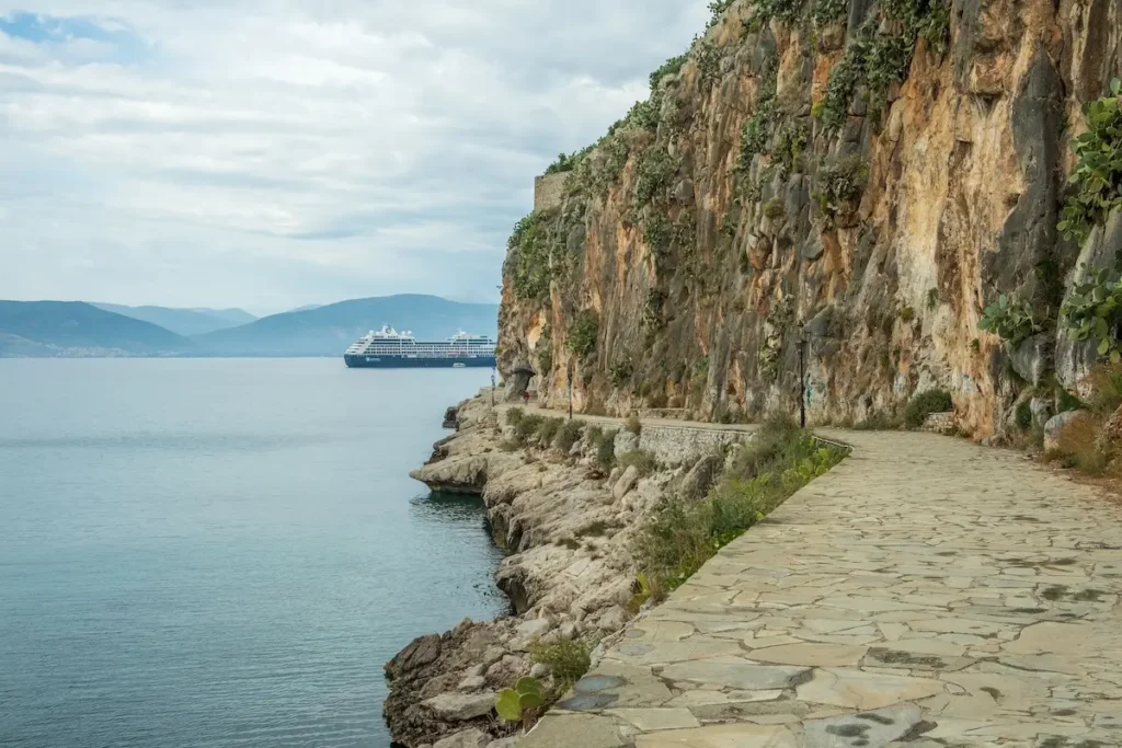 A paved coastal walkway curving along the base of a limestone cliff with the sea on one side.