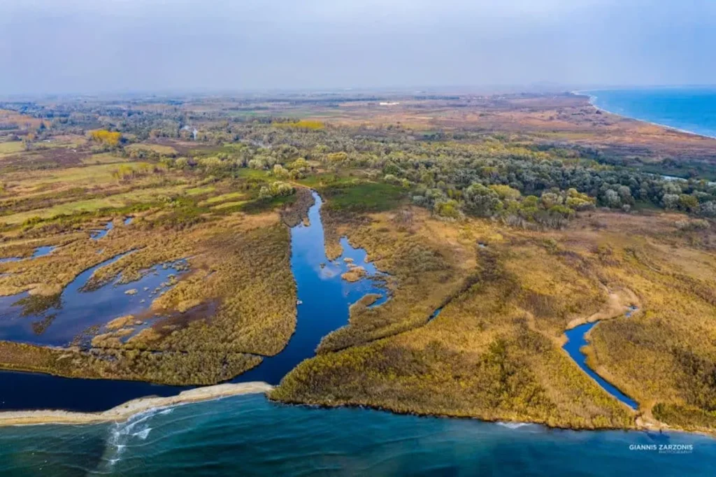 An aerial view of the Nestos River Delta near Keramoti, showing a complex network of shallow water channels, sandbars, and accumulated driftwood meeting the sea.
