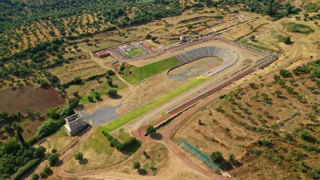 High-angle aerial view of the well-preserved Ancient Messene stadium in Mavromati, Messinia, surrounded by lush greenery.