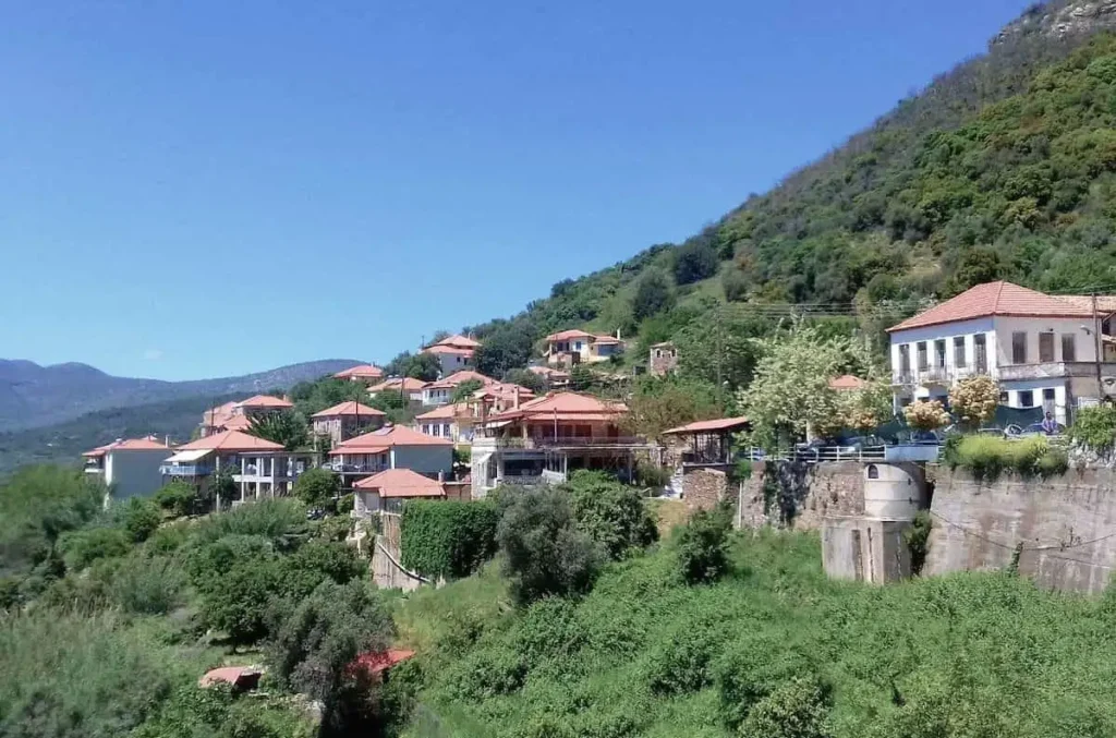 Close-up of traditional stone-built houses with red-tiled roofs in Mavromati, set against the green Messinian landscape.