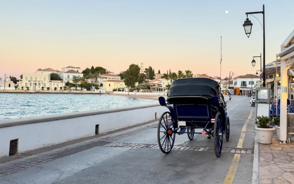 A traditional horse-drawn carriage on a paved coastal road in Spetses.