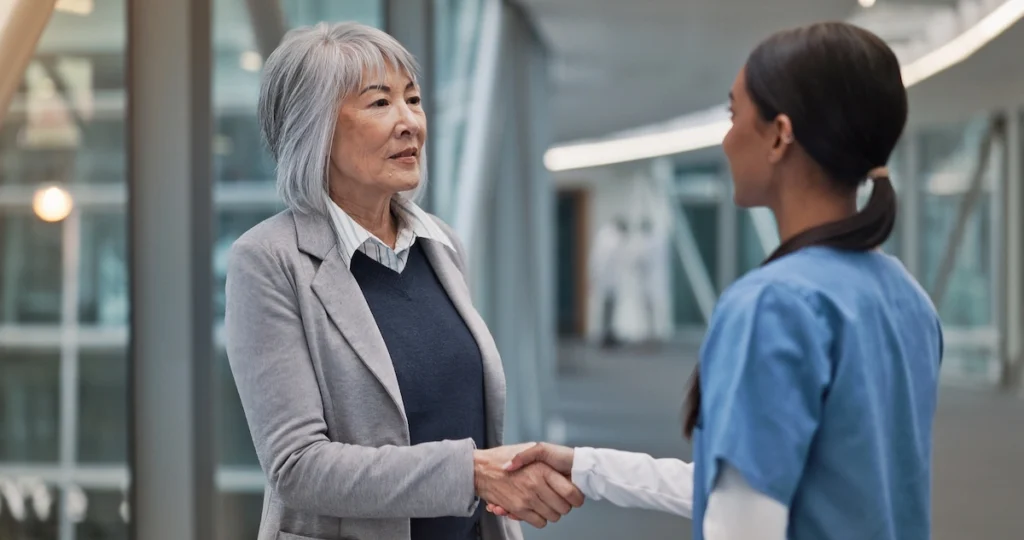 A nurse and a patient shaking hands in a professional medical setting, representing trust and local care standards.