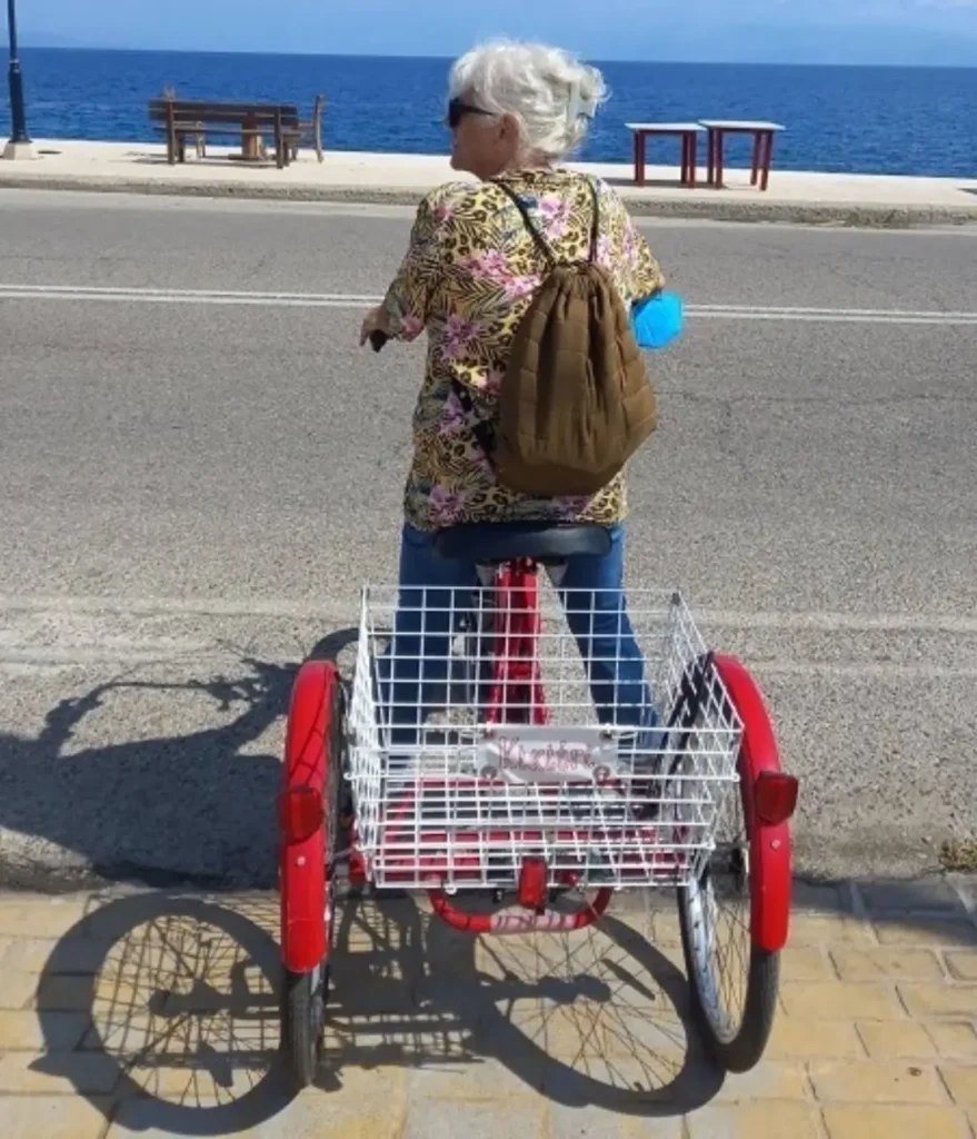 Kiki riding a bicycle with a large rear basket through a quiet village street, looking happy and liberated.
