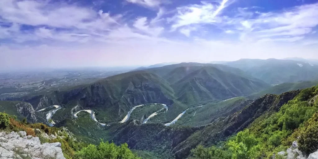 High-angle aerial view of the Nestos River winding in deep, emerald-green curves through steep, forested mountain slopes in Northern Greece.