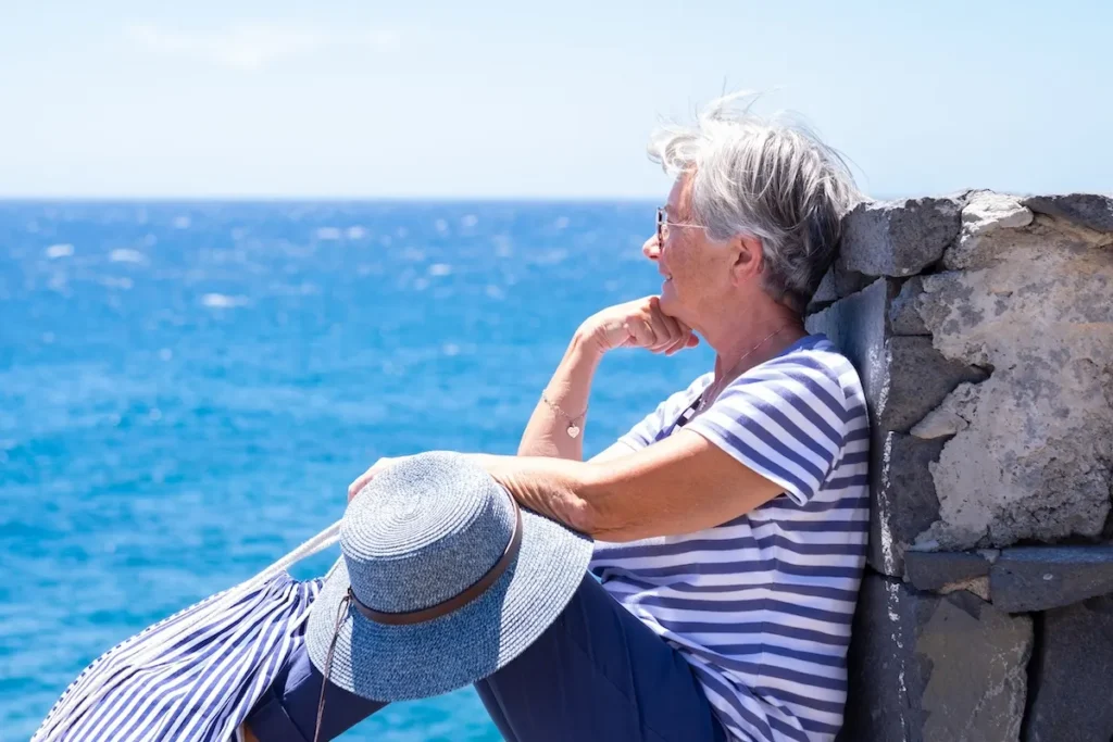 A thoughtful woman standing by the rugged Aegean shoreline, gazing out at the open sea. Used as an illustrative asset for a personal testimony.