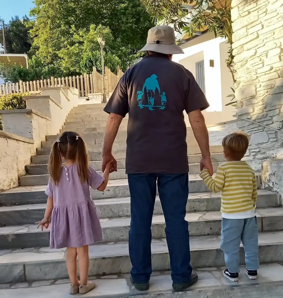 The backs of a Greek retiree, Vangelis Koumarianos, and his grandchildren walking through the streets of his native village in Tinos.