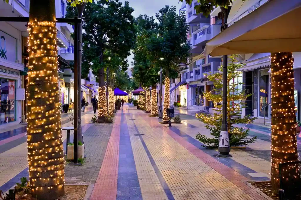 Pedestrian street in Kiato decorated with Christmas lights and festive ornaments, with people enjoying the lively town center.