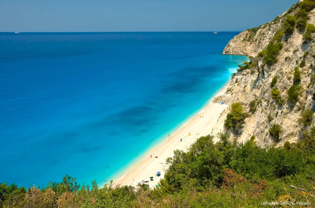 A wide panoramic view of a sweeping white sand beach in Lefkada with deep turquoise Ionian waters.