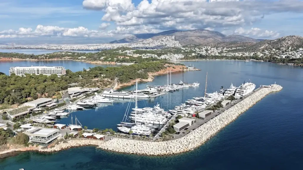 A row of luxury motor yachts and sailing vessels moored at the high-end Astir Marina in Vouliagmeni, viewed from the dock at sunset.