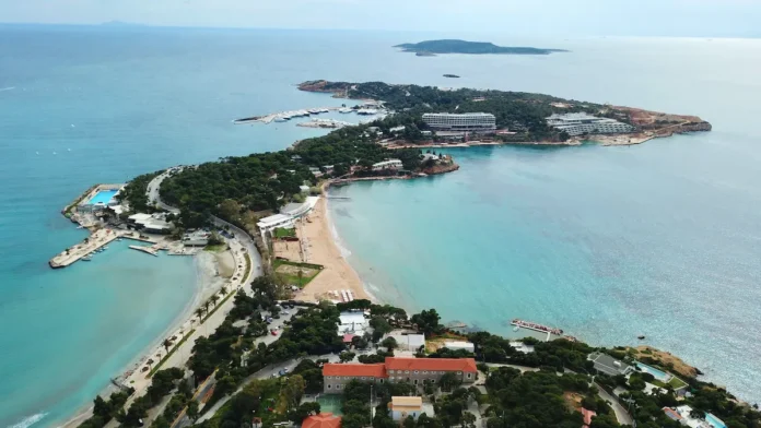 Aerial view of the Laimos peninsula in Vouliagmeni, showing dense pine forests surrounded by the deep blue Saronic Gulf.