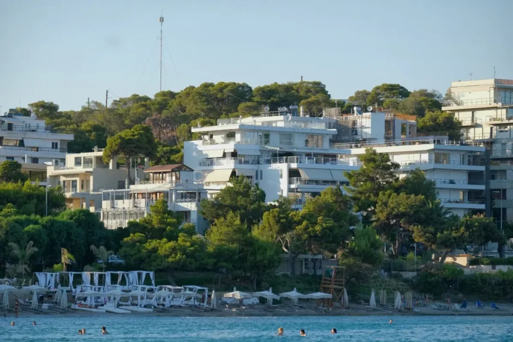 Waterfront view of Vouliagmeni showing a mix of sleek modern luxury villas and classic Greek mid-century apartment buildings.