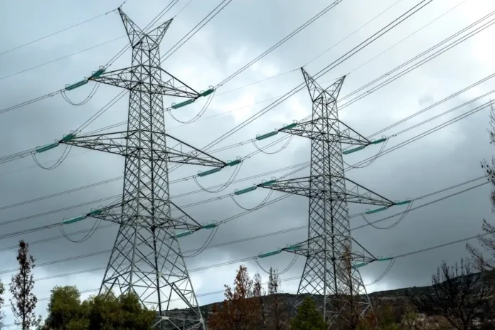 A tall steel lattice electricity transmission pylon standing against a clear sky in Greece.