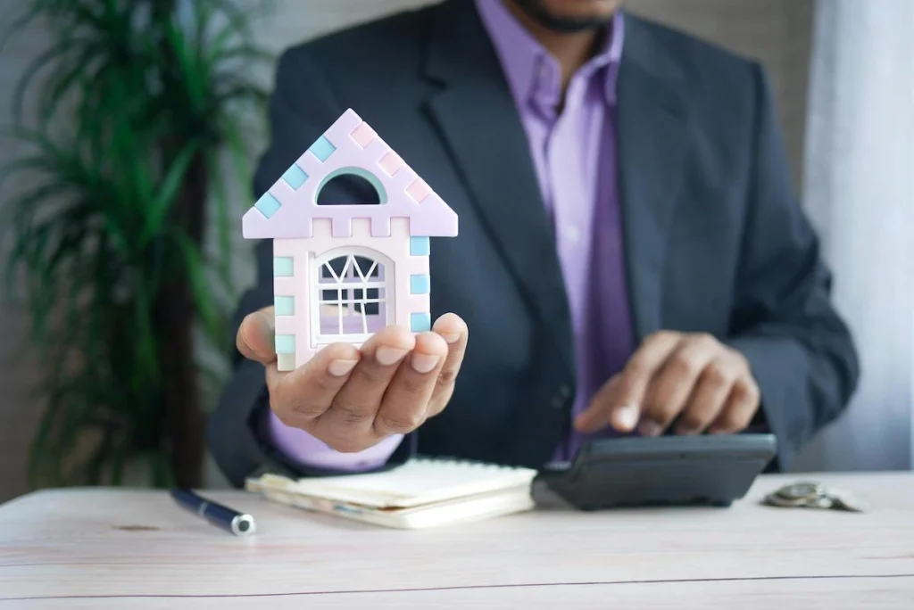 A person's hands holding a white miniature house model, symbolizing property ownership and real estate transactions.