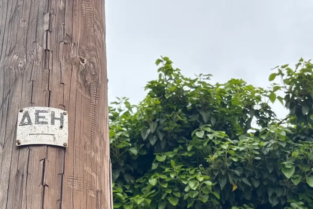 An old utility pole in Greece featuring a weathered, vintage metal DEH logo sign.