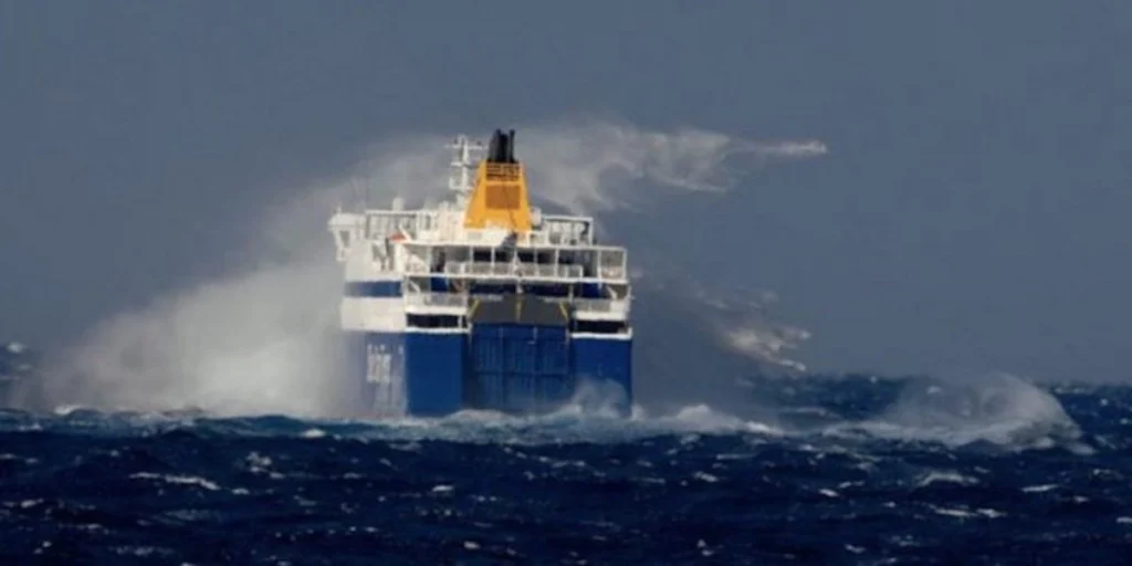 A large blue and white commercial ferry struggling through massive, white-capped grey waves in the open sea.