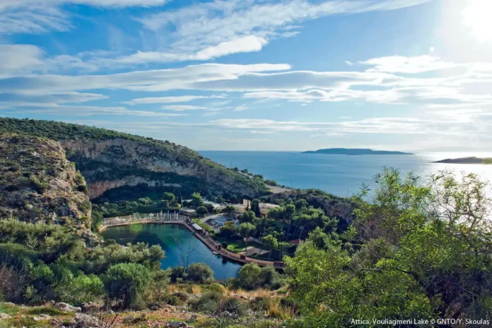 The sunken limestone cavern and emerald-green thermal waters of Lake Vouliagmeni, surrounded by sheer rock faces.