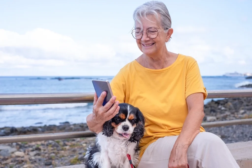 Woman with Cavalier King Charles Spaniel studying on phone by the seaside