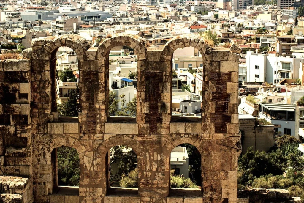 A wide landscape shot of ancient Greek ruins and stone foundations under a soft sky, showing the visible layers of historical architecture and urban development over time.