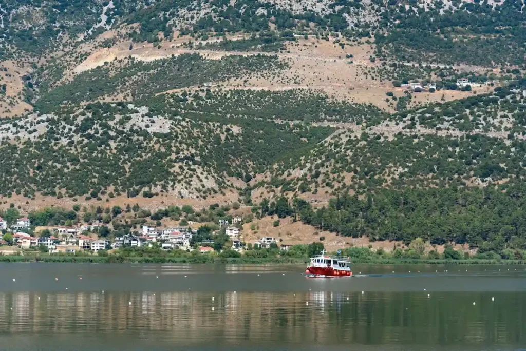 Red boat crossing Lake Pamvotis with mountains in the background in Ioannina