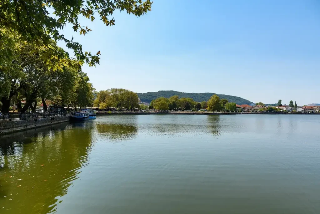Green waters of Lake Pamvotis with trees and moored boats in Ioannina