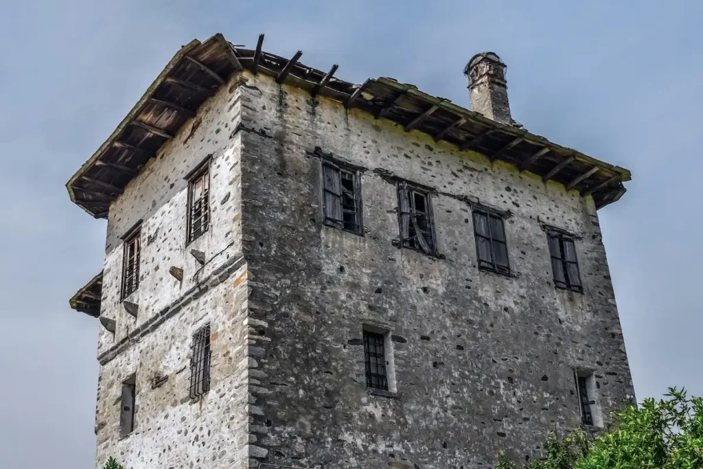 A low-angle shot looking up at an isolated, decaying old stone house against a clear sky, showcasing a collapsing wooden roof and crumbling stone walls with no surrounding buildings.