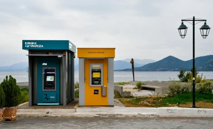 ATMs of the National Bank of Greece and Piraeus Bank positioned along a scenic Aegean coast with sea and mountains in the background.