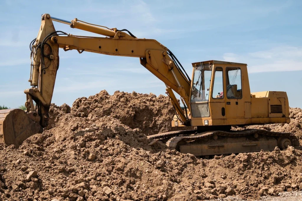 Excavator on a construction plot with mounded earth, no operator present.